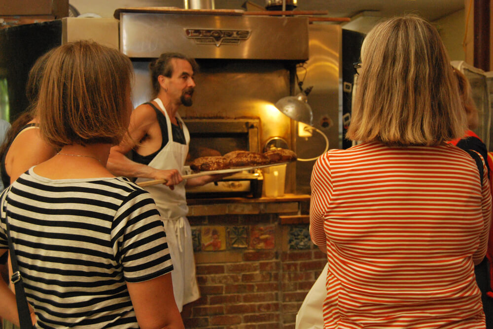 Women looking at a man baking breads on a food tour