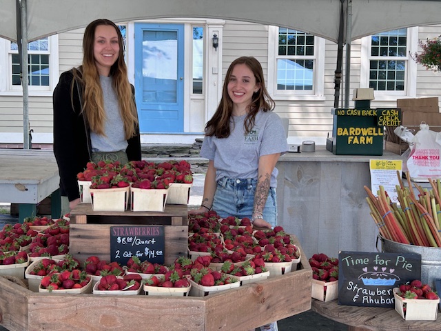 girl farmers at farmstand with fresh ripe strawberries