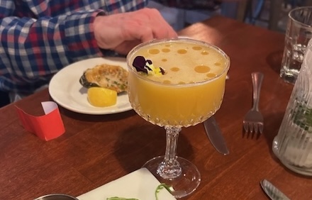 orange cocktail with violet garnish grilled oyster appetizer